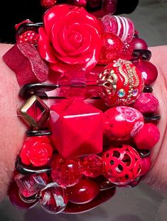 a woman's hand is holding a red bracelet with lots of beads and rings