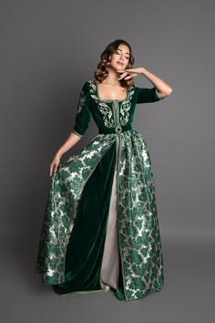 Fitted Velvet Brocade Kaftan Colors: Green, Gold Step into the opulence of the Versaille Kaftan, a true masterpiece of elegance. Luscious green velvet covers the top of the kaftan, embellished with delicate embroidery that subtly adorns the bust. Flower prints extend gracefully along its gold brocade fabric, creating a striking contrast. The lamé under-kaftan brings an additional softness and fluidity to the ensemble, adding a luxurious dimension. The green velvet belt harmoniously completes the Celtic Formal Dress, Fairytale Green Dress, Green Formal Dress With Historical Design, Formal Green Dress With Historical Design, Elegant Ceremonial Floor-length Dress, Elegant Gown With Traditional Drape For Ceremonial Occasions, Elegant Ceremonial Gown With Traditional Drape, Elegant Ceremonial Gown In Traditional Drape, Green Wedding Dress With Historical Design