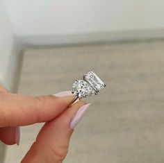 a woman's hand holding an engagement ring with two stones on it and the other side