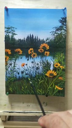 a person is holding a paintbrush in front of an easel with a painting on it