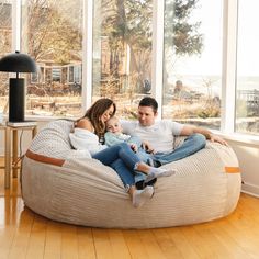 a man and woman are sitting on a bean bag chair in front of large windows