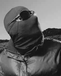 a man wearing a leather jacket and hood with sunglasses on his face looking at the sky