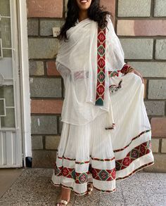 a woman standing in front of a brick wall wearing a white dress with red and green details