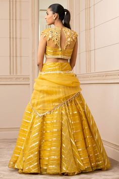 Mustard sheer brocade lehenga with a cascading drape and pearl detailing on the waistband. Paired with embroidered with resham, mirror work blouse. Comes with a matching sheer scarf embellished with fringes.
Component: 3
Pattern: Embroidered
Type Of Work: Mirror
Neckline: Round
Sleeve Type: Cap Sleeves
Fabric: Silk organza brocade stripes
Color: Yellow
Other Details: 
Embroidered blouse
Mirror and resham work
Tassel detail
Closure:
Blouse: Back concealed placket
Occasion: Destination Wedding - A Gold Fitted Organza Pre-draped Saree, Gold Organza Choli With Unstitched Blouse, Gold Organza Choli With Cutdana, Fitted Organza Lehenga With Intricate Embroidery, Gold Organza Lehenga With Unstitched Blouse, Fitted Yellow Tissue Silk Lehenga, Fitted Yellow Tissue Silk Choli, Yellow Fitted Tissue Silk Choli, Unstitched Organza Choli With Traditional Drape