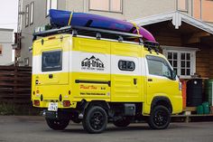 a yellow truck parked in front of a house with a surfboard on the roof