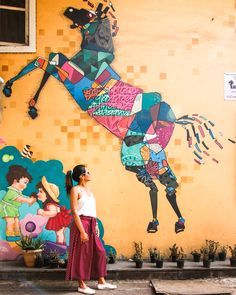 a woman standing in front of a colorful wall with a horse painted on it's side