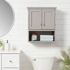 a white toilet sitting under a bathroom mirror next to a sink and cabinet with towels on it