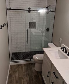 a bathroom with a walk in shower next to a white toilet and wooden flooring