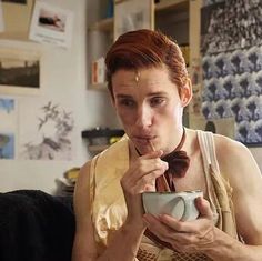 a man with red hair is drinking from a cup while wearing a bow tie and looking at the camera