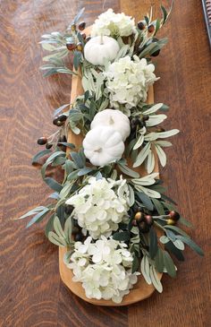 white flowers and greenery are arranged on a wooden board with an acorn centerpiece