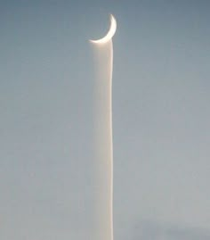 a very tall white pole with a half moon on it's side in the sky