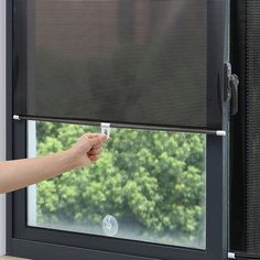 a hand is pulling out the blinds from an open window with trees in the background