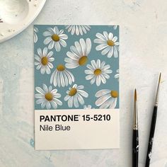 a notepad with daisies on it next to two paintbrushes