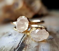 two gold rings with pink crystals on top of each other, sitting on a wooden surface