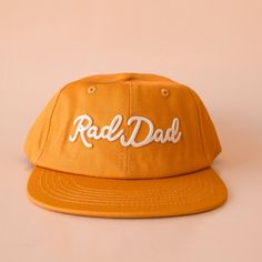 A flat brimmed burnt orange had with white embroidering that reads, Rad Dad. Vintage Orange Snapback Hat, Orange 5-panel Casual Hat, Casual Orange 5-panel Hat, Casual Snapback Hat With Flat Bill For Father's Day, Retro Orange Baseball Cap With Curved Brim, Casual Flat Bill Snapback Hat For Father's Day, Orange Adjustable Snapback Hat With Curved Brim, Retro Hats With Flat Brim For Everyday Wear, Retro Everyday Hats With Flat Brim