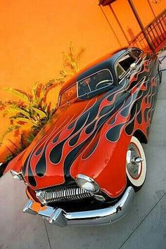 an old red and black car with flames on it's hood parked in front of a building