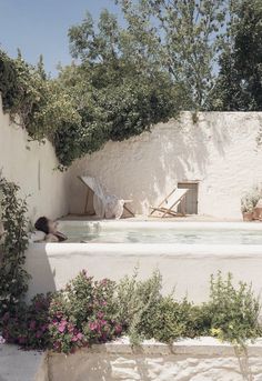 a woman sitting in the middle of a swimming pool surrounded by greenery and flowers