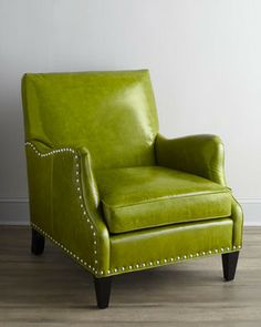 a green leather chair sitting on top of a hard wood floor next to a white wall