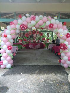 a pink and white balloon arch with flowers on the top is set up for an outdoor party