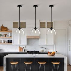 a kitchen with black and white cabinets, wooden stools and hanging lights over the island