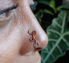 a close up of a person with a nose ring on their nose and leaves in the background