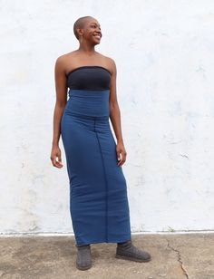 a woman standing in front of a white wall wearing a blue skirt and black top