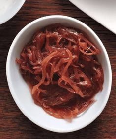 a white bowl filled with red onions on top of a wooden table next to plates