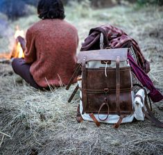 two people sitting next to each other on the ground near a campfire and backpack