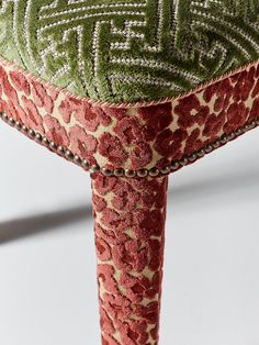 an upholstered stool with a green and red pattern on the top, sitting in front of a white background