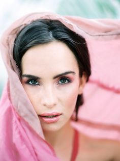 a woman with dark hair and blue eyes wearing a pink shawl over her head