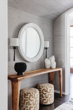 a console table with two stools and a round mirror on the wall