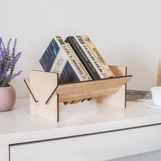 some books are in a wooden holder on a white shelf next to a potted plant