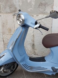 a blue scooter parked next to a stone wall with a mirror on it