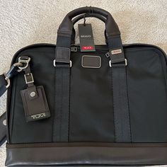 Tumi Unisex Slim Briefcase. Black Ballistic Nylon With Brown Trim. 16” X 12” X 2”. Has Multiple Pockets Inside And Out And Removable/Adjustable Shoulder Strap. Zipped Bottom To Slide On To Rolling Suitcase Handle. Never Used, Pristine Condition. Luxury Black Briefcase With Zipper Closure, Designer Brown Luggage For Business, Designer Brown Business Luggage, Black Leather Luggage With Leather Handles, Classic Black Luggage With Leather Trim, Elegant Nylon Shoulder Bag For Formal Occasions, Black Briefcase With Zipper For Work, Black Laptop Bag With Zipper Closure For Formal Use, Black Laptop Bag With Zipper For Formal Use