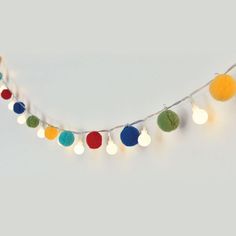 multicolored christmas lights are hanging on a white string with small balls attached to it