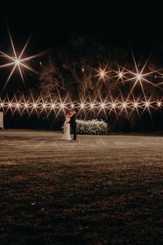 a bride and groom standing in the middle of a field at night with bright lights