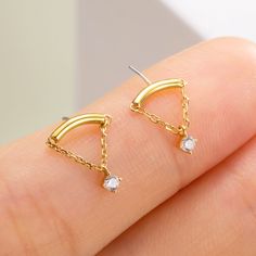 a person's hand holding two small gold earrings with white stones on the bottom