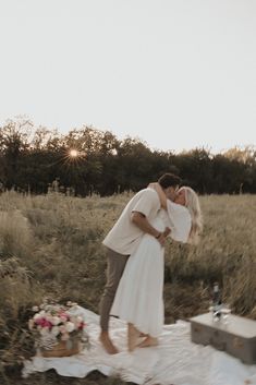 a man and woman kissing on a blanket in a field