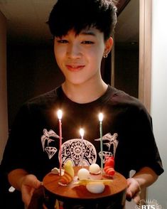 a young boy holding a cake with lit candles on it in front of his face