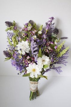 a vase filled with purple and white flowers on top of a table next to a cell phone