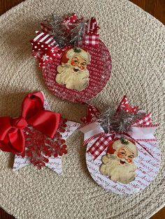 two christmas ornaments on a table with red bows and ribbons around them, sitting on top of a placemat