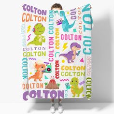 a boy is holding up a blanket with dinosaurs on it and the words cotton written in different colors