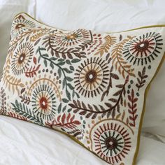 an embroidered pillow on a bed with white sheets