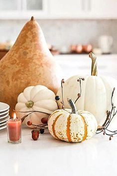 a table topped with lots of white pumpkins and other fall decorating items on top of a kitchen counter