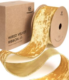 a roll of wired velvet ribbon next to a cardboard box on a white background with gold foil