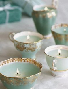 tea cups and saucers with candles in them on a white tableclothed surface