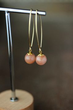 Simple and elegant dangle earrings with natural round pink-brown moonstone/sunstone  10-11 mm beads,  small gold tone bead caps and long gold tone stainless steel oval shape earring hooks. Earring hooks are from nickel free and lead free metal. *The total lenght of earrings is about 54 mm including earring hooks. Since this is a natural stone, the pattern of each bead is unique. I try to choose the most similar beads for each pair. It's believed to be this stone can bring you good luck, happines Elegant Round Sunstone Jewelry, Elegant Sunstone Jewelry, Round Shape, Elegant Apricot Dangle Earrings, Elegant Apricot Earrings For Gift, Elegant Apricot Dangle Jewelry, Elegant Sunstone Jewelry With Natural Stones, Elegant Adjustable Apricot Jewelry, Handmade Elegant Apricot Earrings, Handmade Apricot Earrings Elegant Style