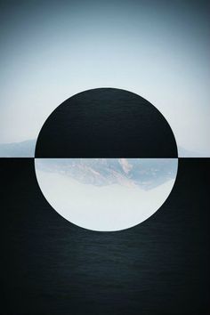 a black and white circle with mountains in the background, as seen from across the water