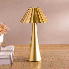 a gold lamp sitting on top of a wooden table next to a vase with flowers