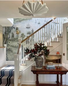 a vase with flowers on top of a table in front of a stair case and wallpaper